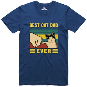 May include: A blue t-shirt with a retro-style graphic of a cat giving a fist bump to a hand. The text "BEST CAT DAD EVER" is printed in yellow on the shirt.