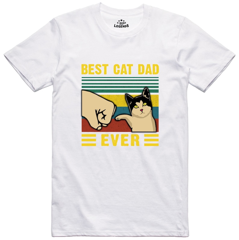 May include: White t-shirt with a retro-style graphic that says "Best Cat Dad Ever". The graphic features a fist bumping a cat with a black and white face.