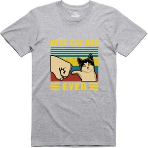 May include: A grey t-shirt with a retro-style graphic that says "Best Cat Dad Ever". The graphic features a cat giving a fist bump to a hand.