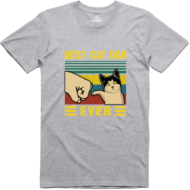 May include: A grey t-shirt with a retro-style graphic that says "Best Cat Dad Ever". The graphic features a cat giving a fist bump to a hand.