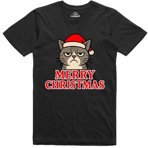 Peut inclure: T-shirt noir avec un chat grincheux portant un bonnet de Père Noël. L'inscription "MERRY CHRISTMAS" est imprimée en rouge avec un contour blanc sous le dessin du chat. Le t-shirt a un col rond et des manches courtes.