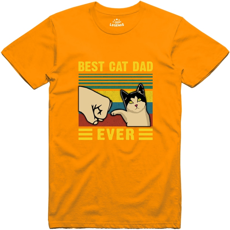 May include: A yellow t-shirt with a retro-style graphic that says "Best Cat Dad Ever". The graphic features a cat giving a fist bump to a hand.
