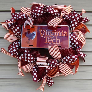 May include: A decorative wreath featuring a Virginia Tech license plate at the center. The wreath is adorned with maroon and white polka dot and striped ribbons, with a turkey graphic on the plate. The wreath is a festive decoration.