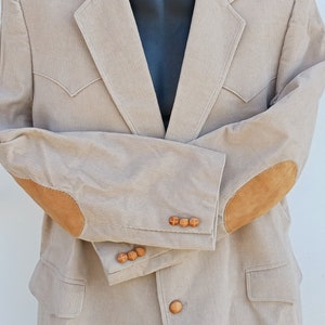 May include: A beige corduroy blazer with suede elbow patches and wooden buttons. The blazer has a classic fit and a single-breasted closure.