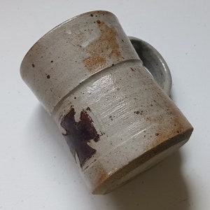 May include: A ceramic mug with a brown and white glaze. The mug has a brown design on the front.