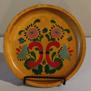May include: A round wooden plate with a painted design of stylized flowers in red, green, blue, and pink on a yellow background.
