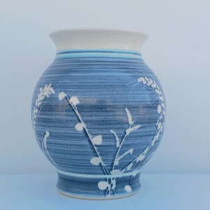 May include: A blue ceramic vase with a white glaze and a floral design. The vase has a rounded body and a flared lip.