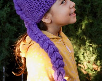 May include: A purple crochet hat with a long, braided extension. The hat is a vibrant shade of purple, and the braid ends in a tassel. The hat is likely handmade and suitable for children.