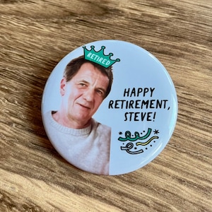 Peut inclure: Un bouton rond et blanc avec la photo d'un homme portant une couronne avec le mot "Retraité". Le bouton dit "Joyeuse retraite, Steve !" avec des confettis verts et jaunes. Le bouton est sur une surface en bois.