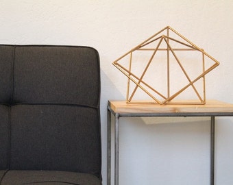 May include: A gold geometric sculpture sits on a wooden top side table with a black metal frame. The table is next to a dark gray sofa.
