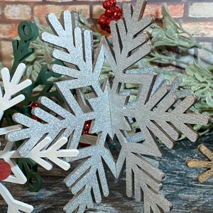 May include: A silver glitter snowflake ornament with a woodgrain texture. The snowflake is a 3D design with multiple layers.
