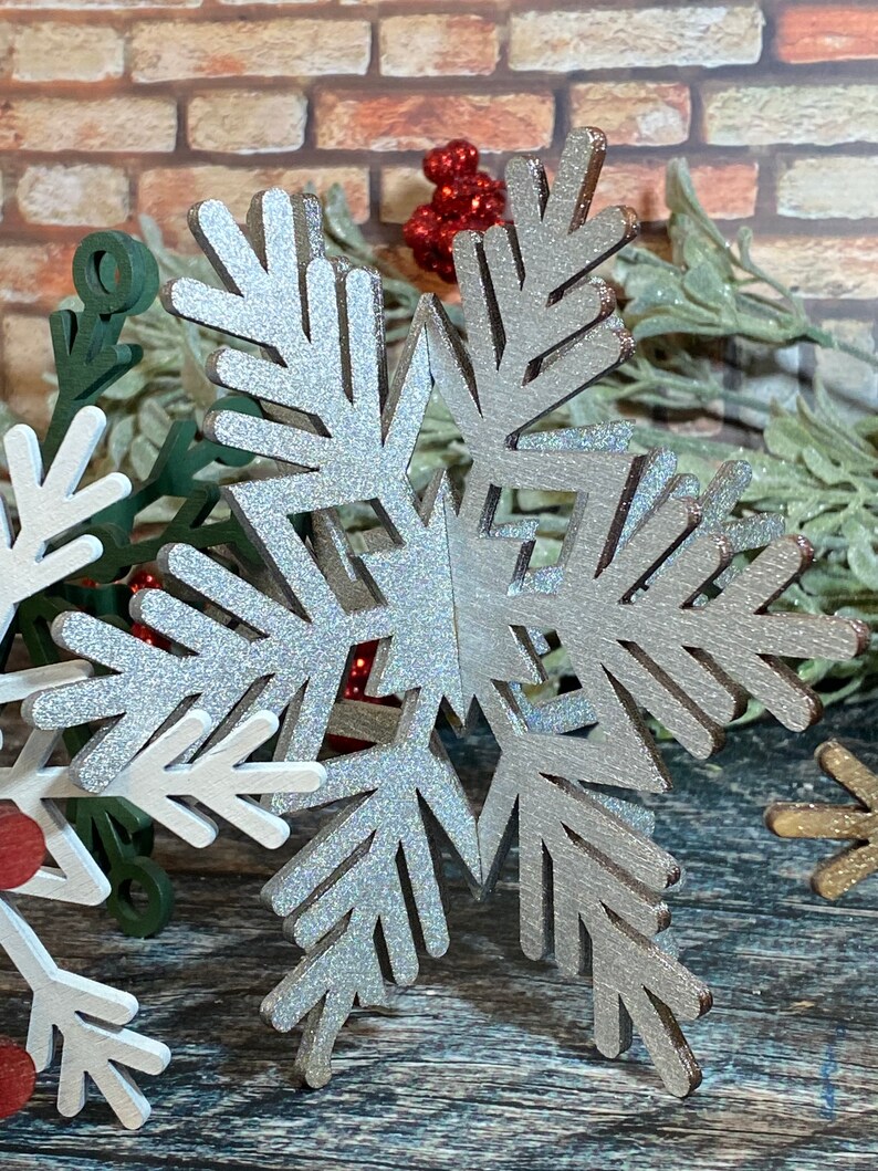 May include: A silver glitter snowflake ornament with a woodgrain texture. The snowflake is a 3D design with multiple layers.