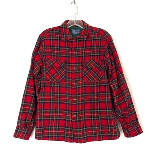 Puede incluir: Una camisa a cuadros roja con detalles verdes y azul marino. La camisa tiene dos bolsillos delanteros y un cuello. La prenda está colgada sobre un fondo blanco.