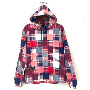 May include: A patchwork hooded jacket in red, white, and blue plaid patterns. The jacket features a drawstring hood, a front pocket, and a button-down placket. A small label is sewn on the lower left side.