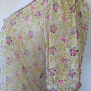 K&ouml;nnte beinhalten: Eine wei&szlig;e Bluse mit kurzen &Auml;rmeln und einem Blumendruck in Rosa-, Gr&uuml;n- und Braunt&ouml;nen. Die Bluse hat einen runden Ausschnitt und einen gerafften &Auml;rmel.