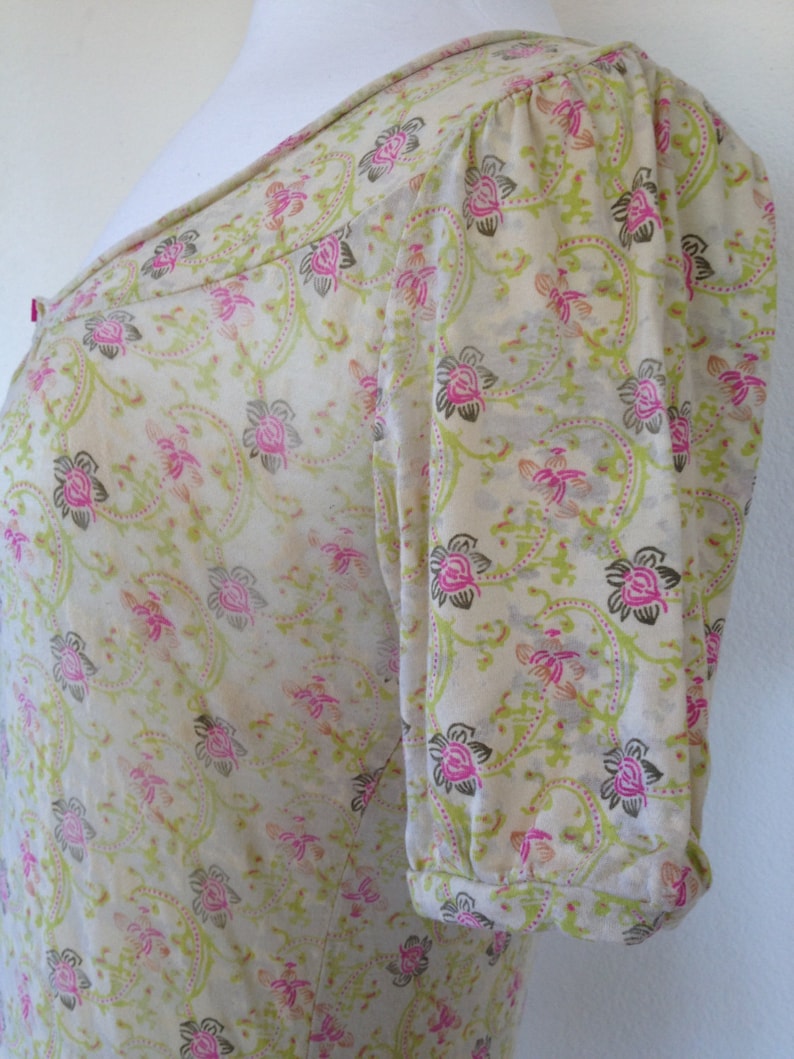K&ouml;nnte beinhalten: Eine wei&szlig;e Bluse mit kurzen &Auml;rmeln und einem Blumendruck in Rosa-, Gr&uuml;n- und Braunt&ouml;nen. Die Bluse hat einen runden Ausschnitt und einen gerafften &Auml;rmel.