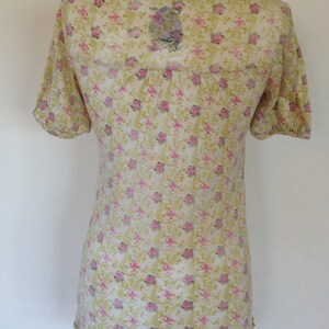 K&ouml;nnte beinhalten: Eine hellgelbe, halbtransparente Bluse mit Blumenmuster. Die Bluse hat einen runden Ausschnitt und kurze &Auml;rmel.