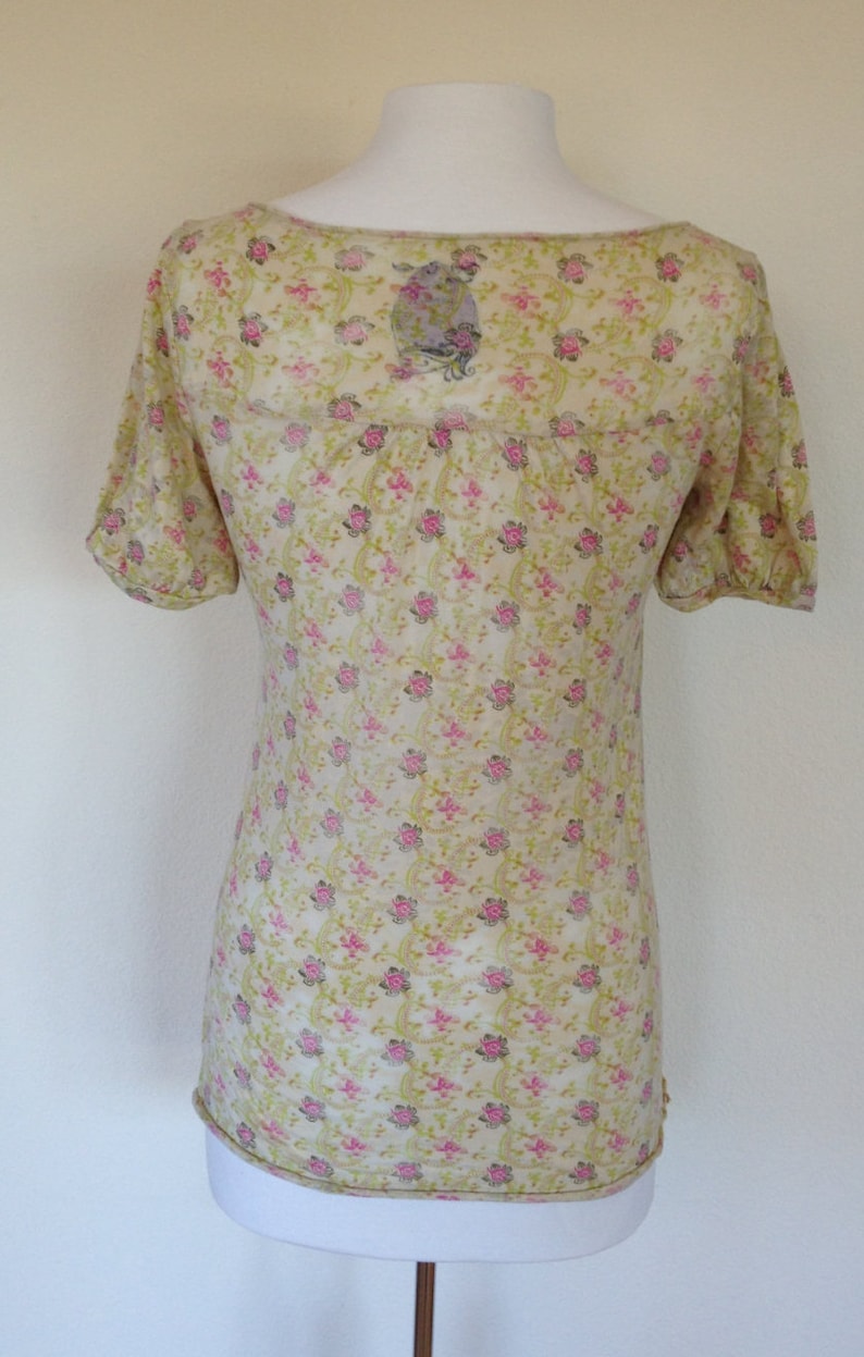 K&ouml;nnte beinhalten: Eine hellgelbe, halbtransparente Bluse mit Blumenmuster. Die Bluse hat einen runden Ausschnitt und kurze &Auml;rmel.