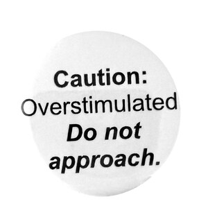 May include: A white circular button with black text that reads "Caution: Overstimulated Do not approach."