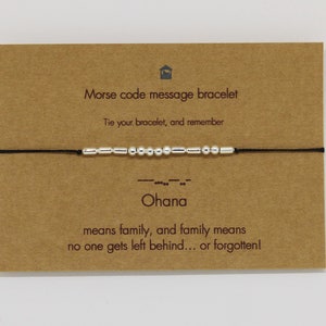 May include: A Morse code message bracelet with silver beads spelling "Ohana" on a black cord. The bracelet is displayed on a brown card with text that reads "Ohana means family, and family means no one gets left behind... or forgotten!"