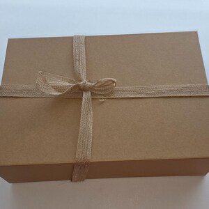 May include: A rectangular, brown cardboard gift box tied with a natural twine ribbon and bow. The box is closed and ready for gifting. The twine is wrapped around the box and tied in a bow on top.