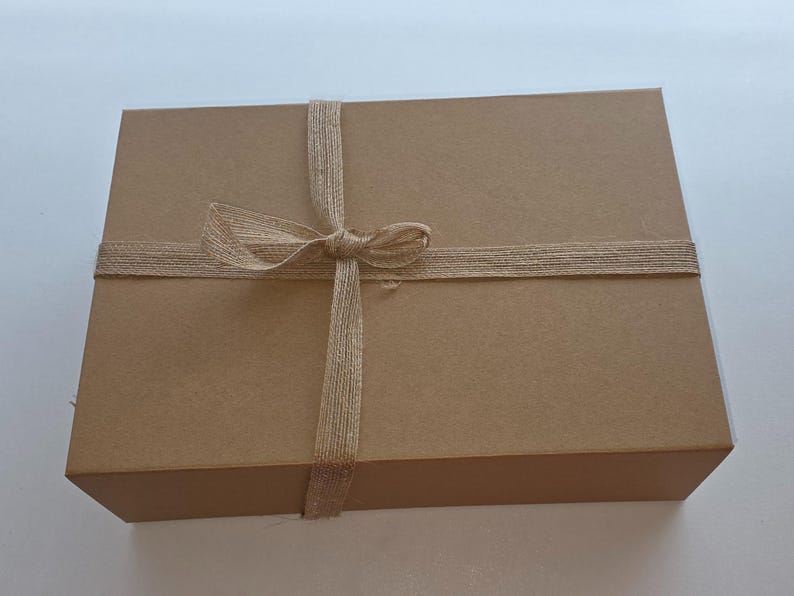 May include: A rectangular, brown cardboard gift box tied with a natural twine ribbon and bow. The box is closed and ready for gifting. The twine is wrapped around the box and tied in a bow on top.