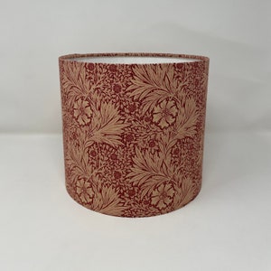 May include: A red and gold floral patterned lampshade. The shade is cylindrical and has a white lining.