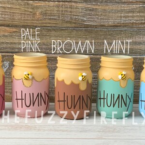 Peut inclure: Cinq bocaux en verre peints en vieux rose, rose p&acirc;le, marron, menthe et bleu p&acirc;le. Chaque bocal pr&eacute;sente un motif de coul&eacute;e de miel jaune sur le dessus, une petite figurine d'abeille et le mot "HUNNY" &eacute;crit en noir sur le devant.