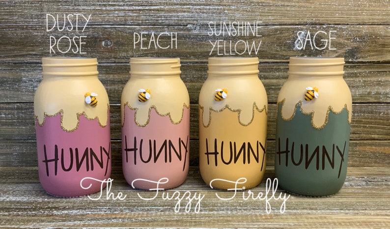 Peut inclure: Quatre pots en verre peints dans diff&eacute;rentes couleurs avec un motif de miel qui coule et une abeille sur le dessus. Les pots sont &eacute;tiquet&eacute;s "Hunny" en lettres noires. Les couleurs sont rose poussi&eacute;reux, p&ecirc;che, jaune soleil et sauge.