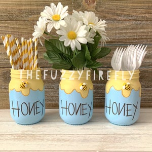 Peut inclure: Trois pots en verre bleus avec des motifs d'abeilles jaunes et noires et le mot "Honey" &eacute;crit sur chaque pot. Les pots sont remplis de pailles, de fourchettes en plastique blanches et d'un bouquet de marguerites blanches.