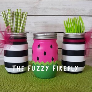 Puede incluir: Tres frascos de vidrio con tapas plateadas. Dos frascos tienen rayas horizontales negras y blancas con lazos de tul rosa. Un frasco est&aacute; pintado de rosa con semillas negras en forma de gota y una base verde. El texto THE FUZZY FIREFLY est&aacute; presente.