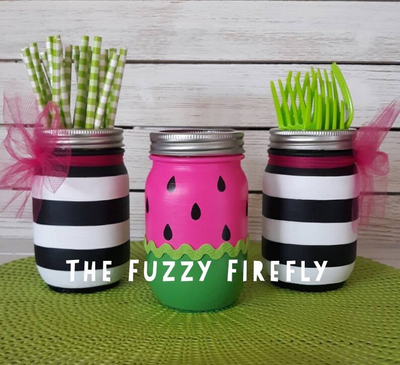 Puede incluir: Tres frascos de vidrio con tapas plateadas. Dos frascos tienen rayas horizontales negras y blancas con lazos de tul rosa. Un frasco est&aacute; pintado de rosa con semillas negras en forma de gota y una base verde. El texto THE FUZZY FIREFLY est&aacute; presente.