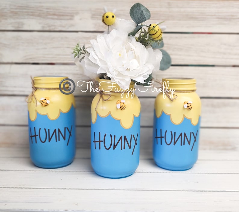 Peut inclure: Trois pots en verre bleus avec des couvercles jaunes et des nids d'abeilles peints dessus. Chaque pot porte le mot "Hunny" &eacute;crit en noir sur le devant. Les pots sont d&eacute;cor&eacute;s de petites figurines d'abeilles jaunes et noires.