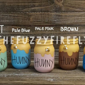 Peut inclure: Cinq bocaux en verre peints en menthe, bleu p&acirc;le, rose p&acirc;le, marron et bleu. Chaque bocal pr&eacute;sente un motif de coul&eacute;e jaune sur le dessus, une petite figurine d'abeille et le mot HUNNY &eacute;crit en noir. Des &eacute;tiquettes identifient chaque couleur.