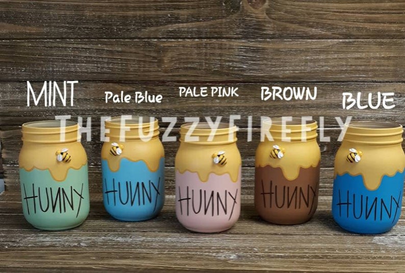 Peut inclure: Cinq bocaux en verre peints en menthe, bleu p&acirc;le, rose p&acirc;le, marron et bleu. Chaque bocal pr&eacute;sente un motif de coul&eacute;e jaune sur le dessus, une petite figurine d'abeille et le mot HUNNY &eacute;crit en noir. Des &eacute;tiquettes identifient chaque couleur.