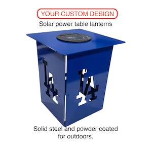 May include: A blue powder-coated steel solar power table lantern featuring a cutout LA logo on the sides. The top surface includes a circular solar panel. Text on the image reads: YOUR CUSTOM DESIGN, Solar power table lanterns, Solid steel and powder coated for outdoors.
