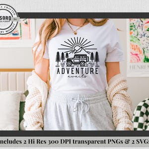 May include: White t-shirt with a black graphic design featuring a mountain, sun, trees, and a 4x4 vehicle. The words "ADVENTURE awaits" are below the graphic. The shirt is part of a design shop collection.