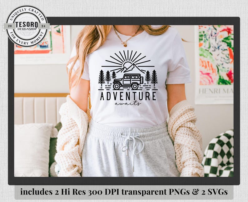 May include: White t-shirt with a black graphic design featuring a mountain, sun, trees, and a 4x4 vehicle. The words "ADVENTURE awaits" are below the graphic. The shirt is part of a design shop collection.
