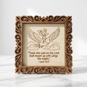 May include: A square wooden wall plaque with an ornate, laser-cut scrollwork frame. The centre panel features an engraved illustration of a child riding a large eagle above clouds, with the text: "Those who wait on the Lord shall mount up with wings like eagles." - Isaiah 40:31.