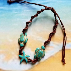 May include: Brown braided anklet with turquoise turtle and starfish charms. The anklet features two turtle charms and a starfish charm, all in a vibrant turquoise color. The braided cord is a rich brown.