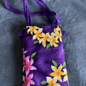 May include: A purple crossbody bag with a floral pattern. The bag features yellow and pink flowers with green leaves. It has a zipper closure and a purple strap.