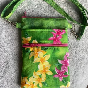 May include: A green crossbody bag with a floral pattern of yellow and pink flowers. The bag has a pink zipper and a green strap. The bag is made of fabric and has a small pocket on the front.