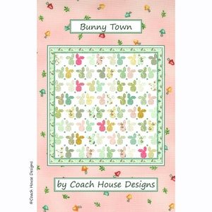 May include: A quilt pattern featuring a repeating design of bunny rabbits in various colors and patterns. The quilt is surrounded by a border of green leaves and orange mushrooms. The title "Bunny Town" and the text "by Coach House Designs" are printed at the top and bottom of the image.