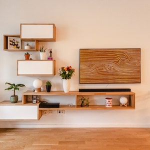 May include: A white and brown wooden shelf unit with a TV mounted on the wall above it. The shelf unit has a variety of items on it, including plants, a vase of flowers, and a decorative object. The TV is a flat screen and is turned off.