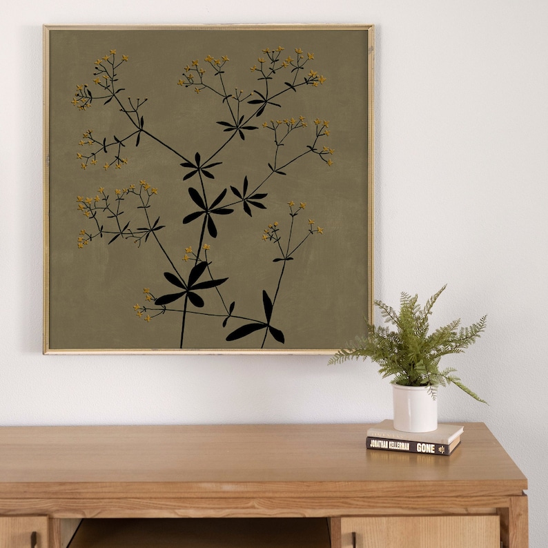 May include: A framed print of a botanical illustration featuring a black silhouette of a plant with yellow flowers on a muted green background.