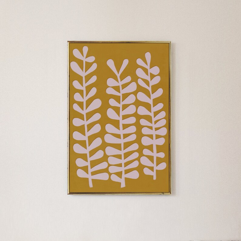 Op de afbeelding: Een ingelijst drukwerk met een mosterdgele achtergrond en drie roze gestileerde plantsilhouetten.