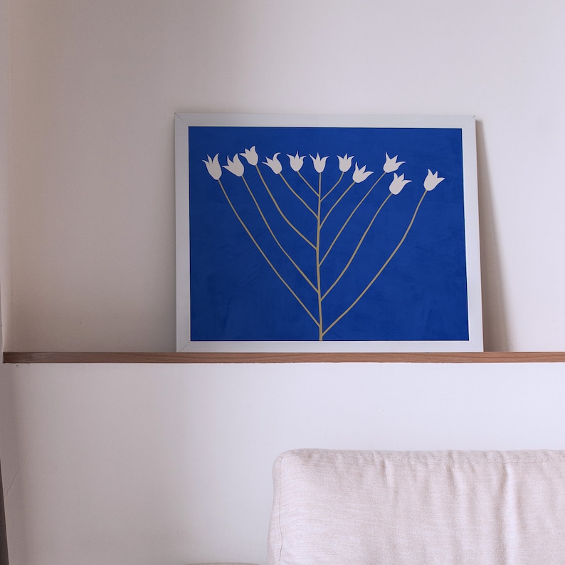 May include: A framed print of a stylized white flower design on a blue background. The flowers are arranged in a symmetrical pattern, resembling a stylized tree.