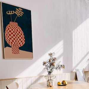 May include: A framed print of a red and white checkered vase with a gold stem and leaves on a blue background.