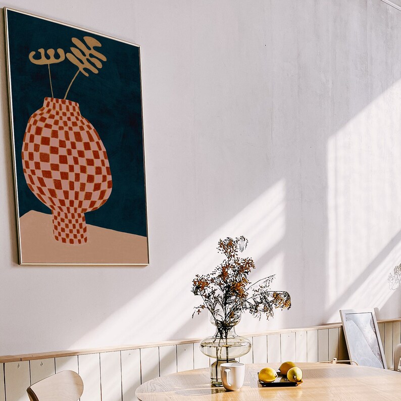May include: A framed print of a red and white checkered vase with a gold stem and leaves on a blue background.
