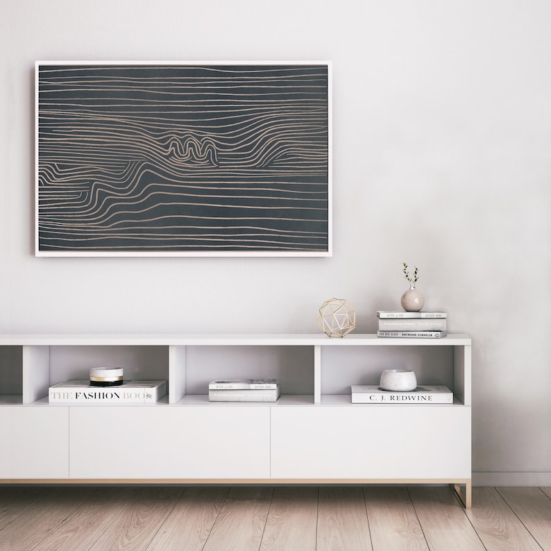 May include: A white media console with three shelves, featuring books and decorative objects. A framed abstract art print with gold lines on a dark background hangs above the console.